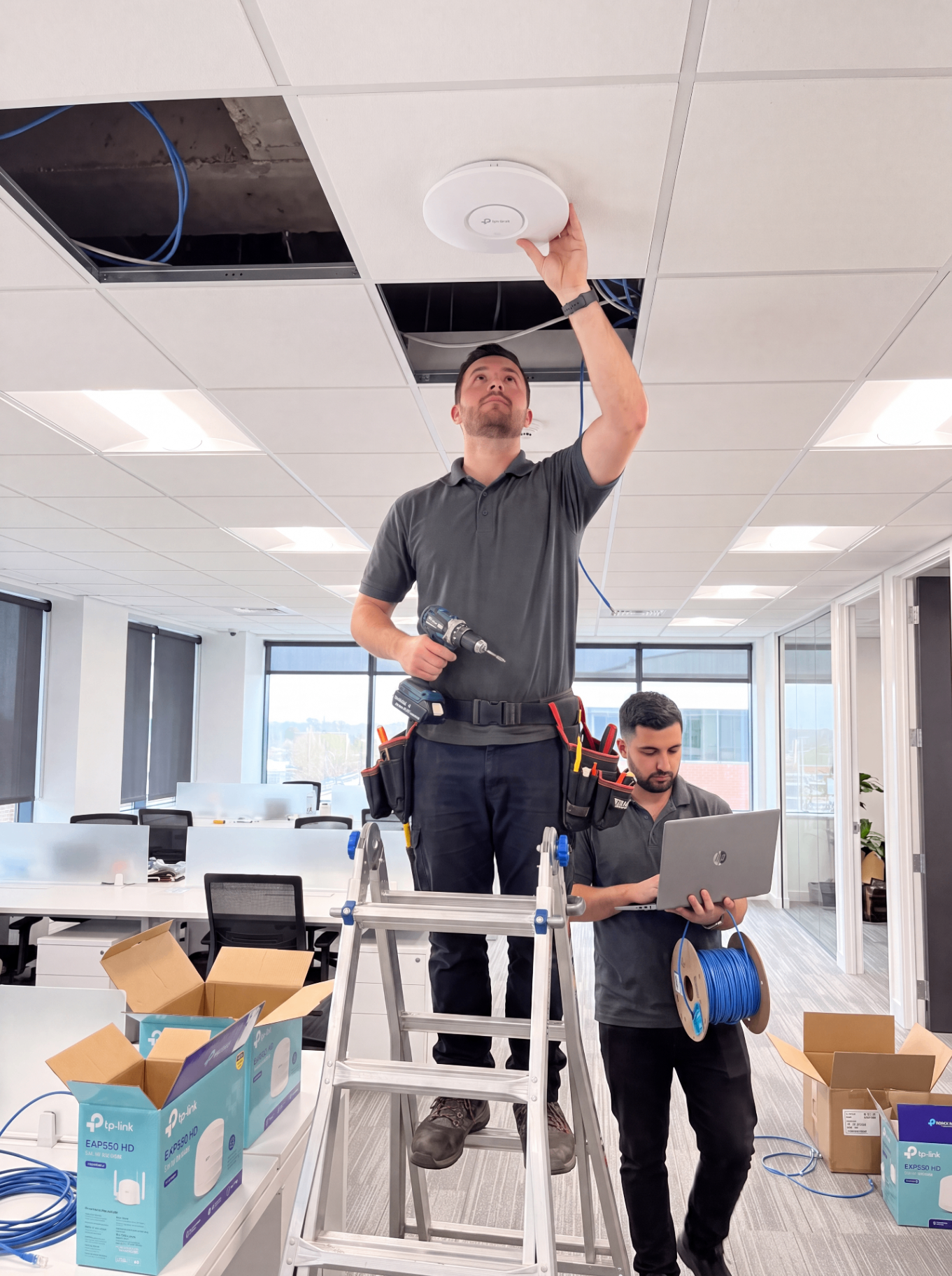 Technicians installing a ceiling wireless access point with a laptop and Ethernet cable